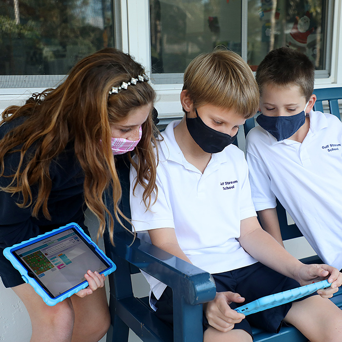 private lower school students wearing masks reading on their ipads outside